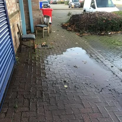 Commercial block-paved passage before cleaning, with standing water, weeds and leaf litter